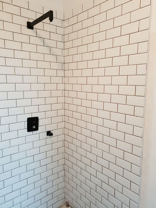 Douche carrelée de faïence blanche de type métro avec accessoires noirs ; pommeau de douche et robinet.