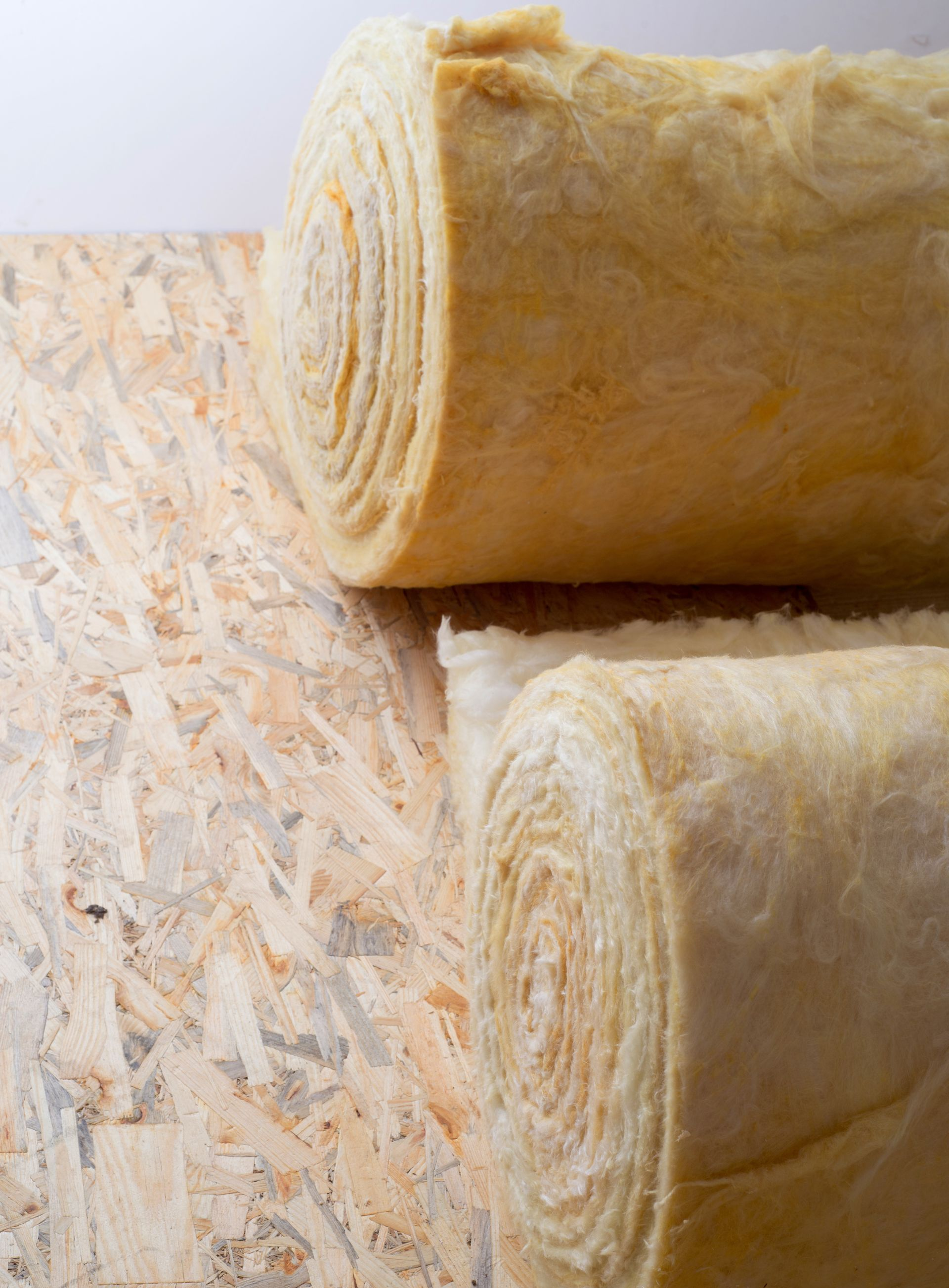 Deux rouleaux d'isolant jaune sur un panneau de bois.