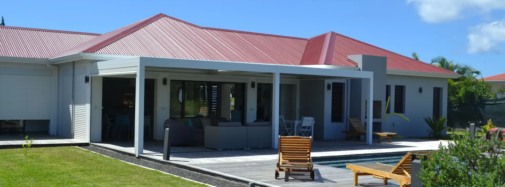 Une maison de plain-pied avec un toit rouge, un patio et une piscine, par une journée ensoleillée.