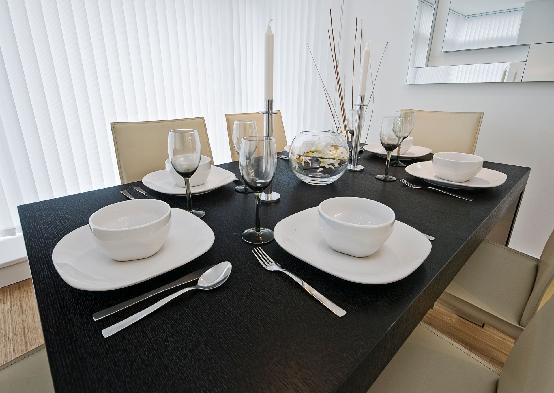 Table à manger dressée avec assiettes, couverts et verres, agrémentée de bougies décoratives et de fleurs.
