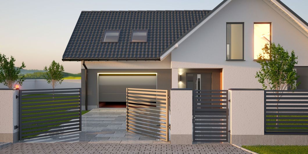 Une maison au toit gris, avec un garage et une entrée fermée par un portail, donnant sur une petite cour avant arborée.