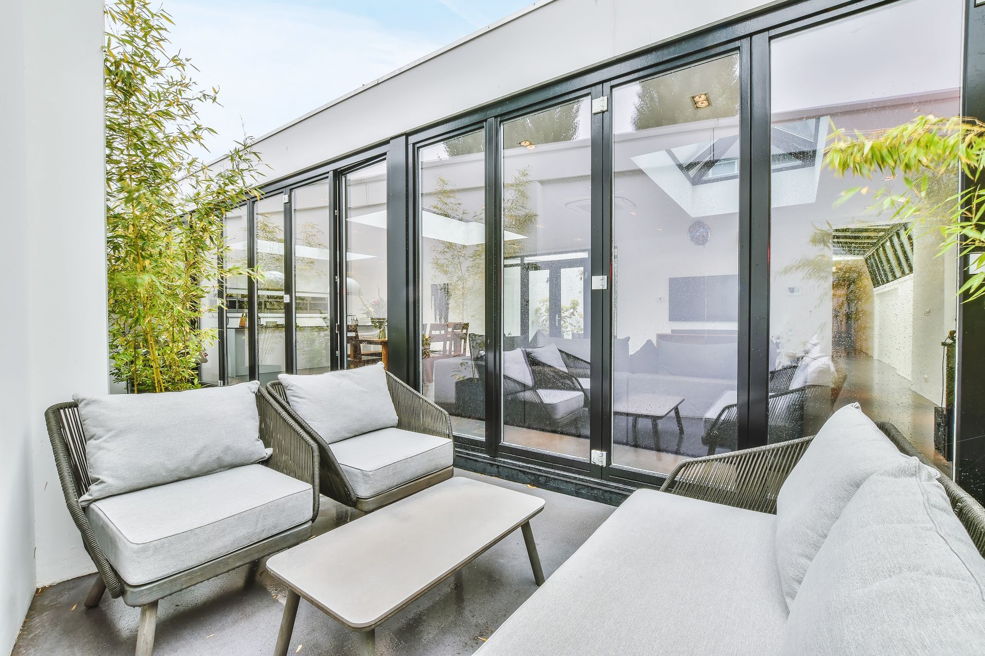 Coin salon extérieur avec mobilier gris, portes vitrées et verdure.