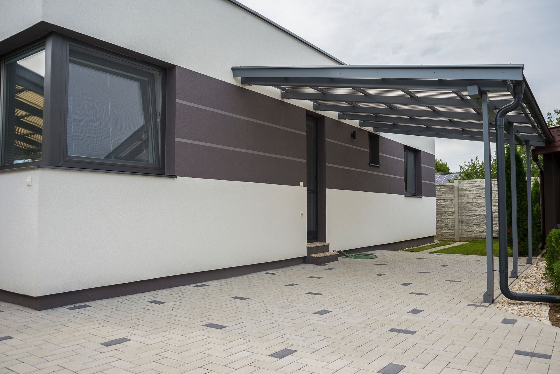 Maison moderne avec extérieur gris foncé et blanc, abri voiture et allée à motifs.