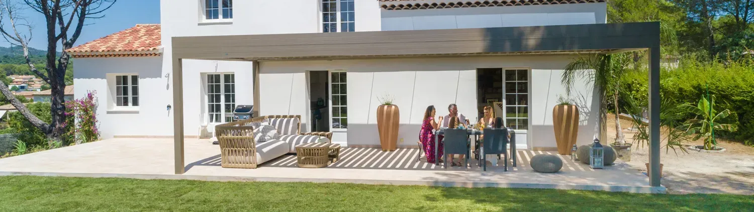 Un groupe de personnes assises autour d'une table sur la terrasse d'une maison blanche avec une pelouse verte.