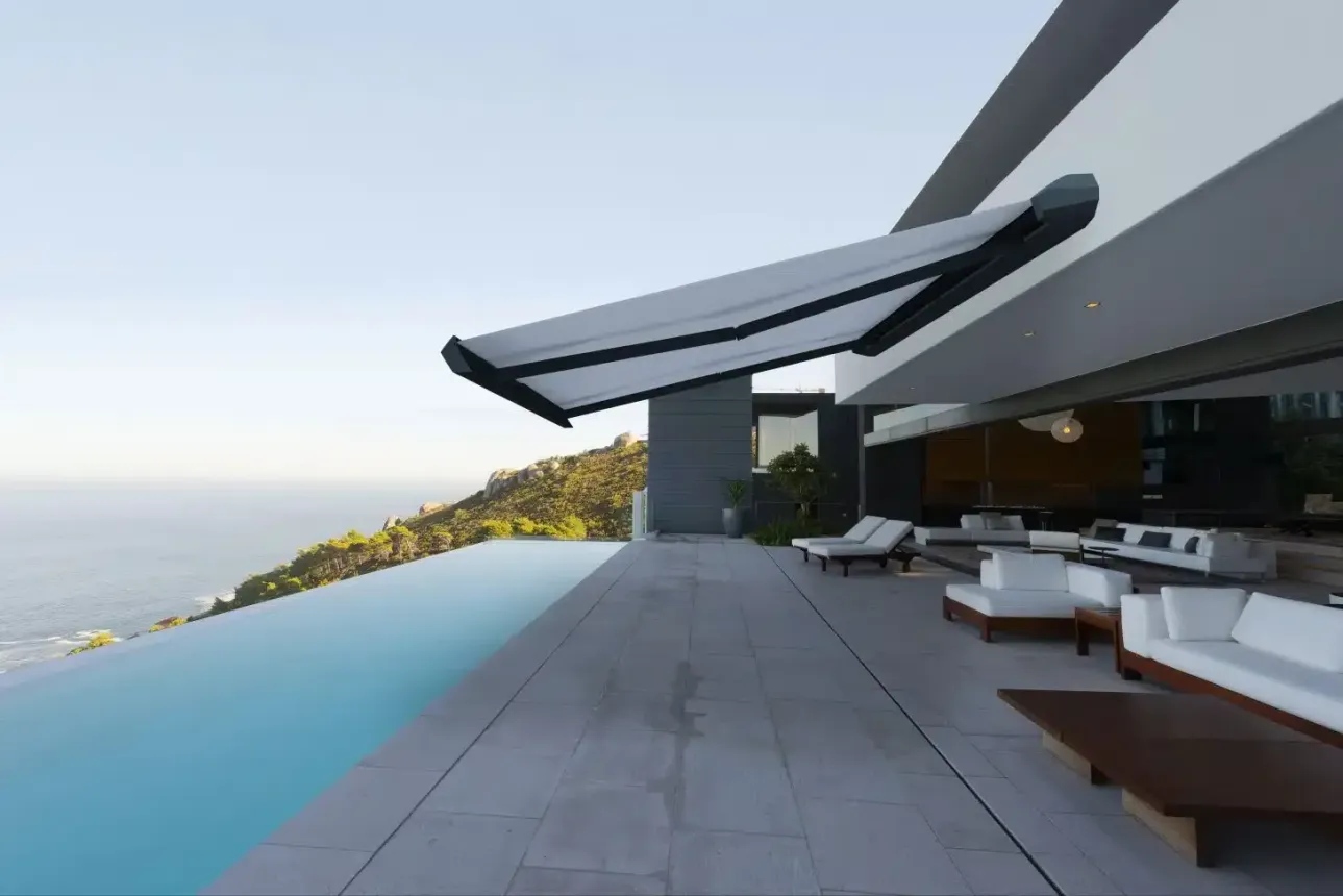 Maison moderne avec auvent ouvert donnant sur une piscine et l'océan. Mobilier de salon visible.