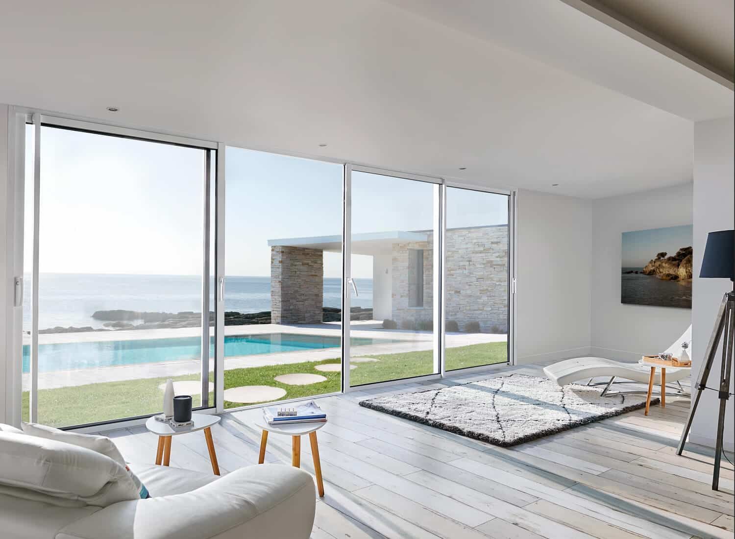 Salon lumineux avec de grandes baies vitrées donnant sur une piscine et l'océan.