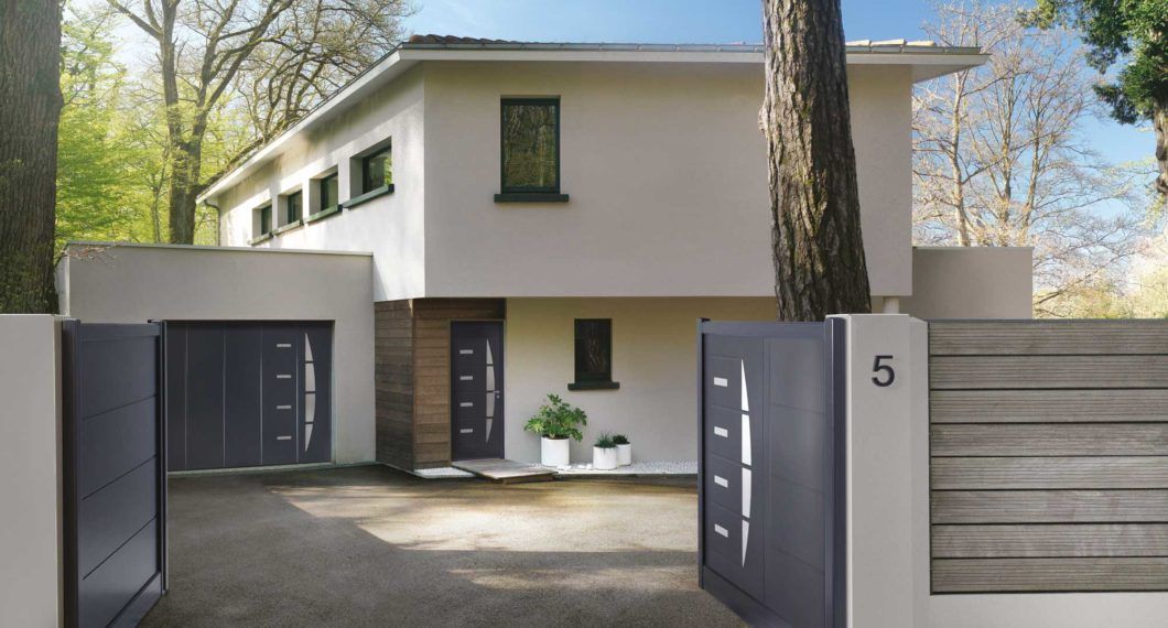 Maison moderne à deux étages avec portail, allée et porte d'entrée gris. Numéro 5 sur un pilier, clôture en bois.