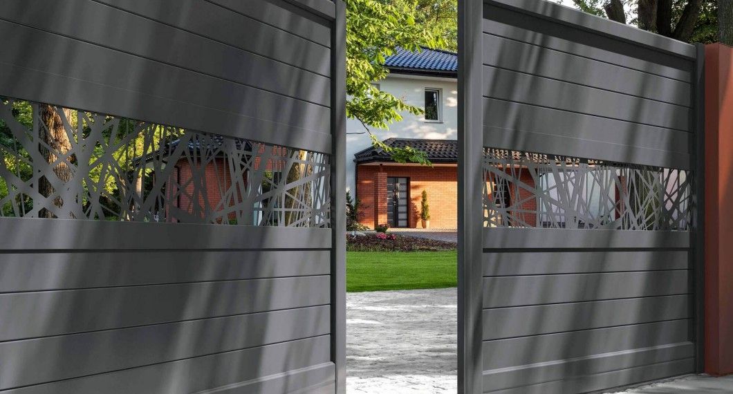 Portail en métal gris orné d'un motif d'arbre, s'ouvrant sur une maison et un jardin.