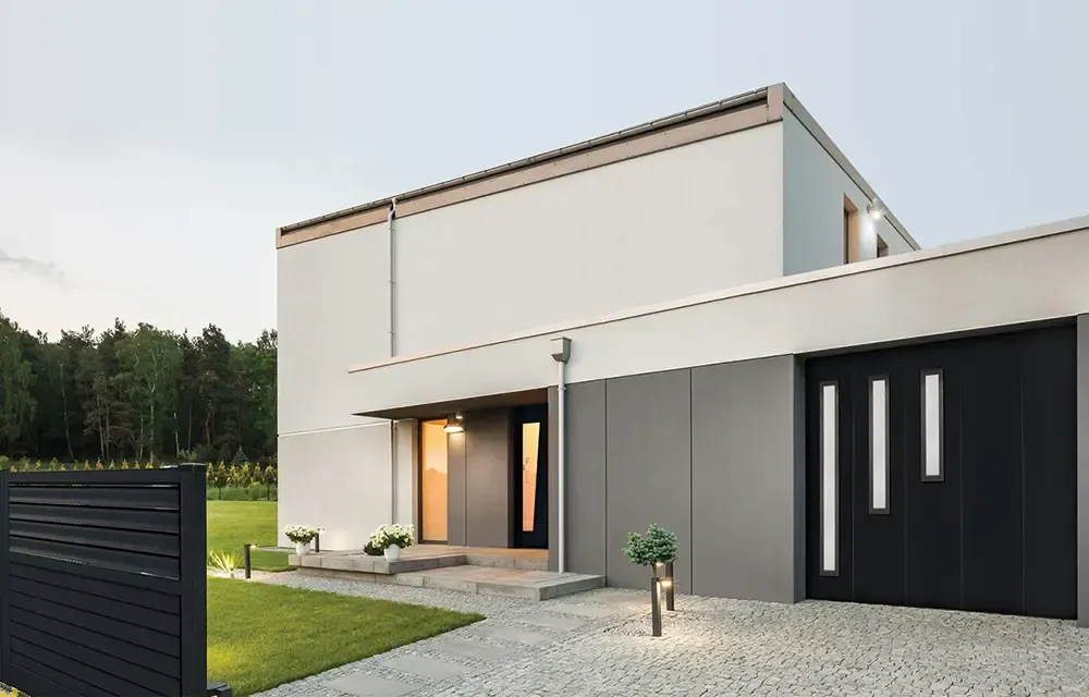 Maison moderne blanche et grise avec des touches de noir, porte d'entrée et porte de garage. Allée, pelouse et clôture en galets.