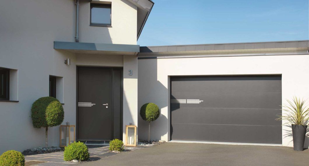 Maison moderne à l'extérieur gris, avec porte de garage et porte d'entrée.
