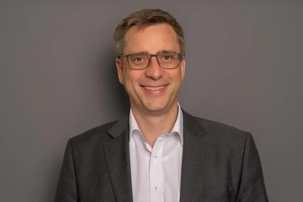 Ein Mann im Anzug und mit Brille lächelt in die Kamera.