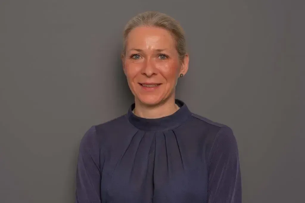 Eine Frau in einem blauen Hemd lächelt in die Kamera.