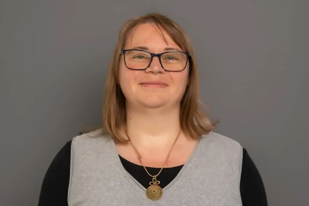 Eine Frau mit Brille und Halskette lächelt in die Kamera.