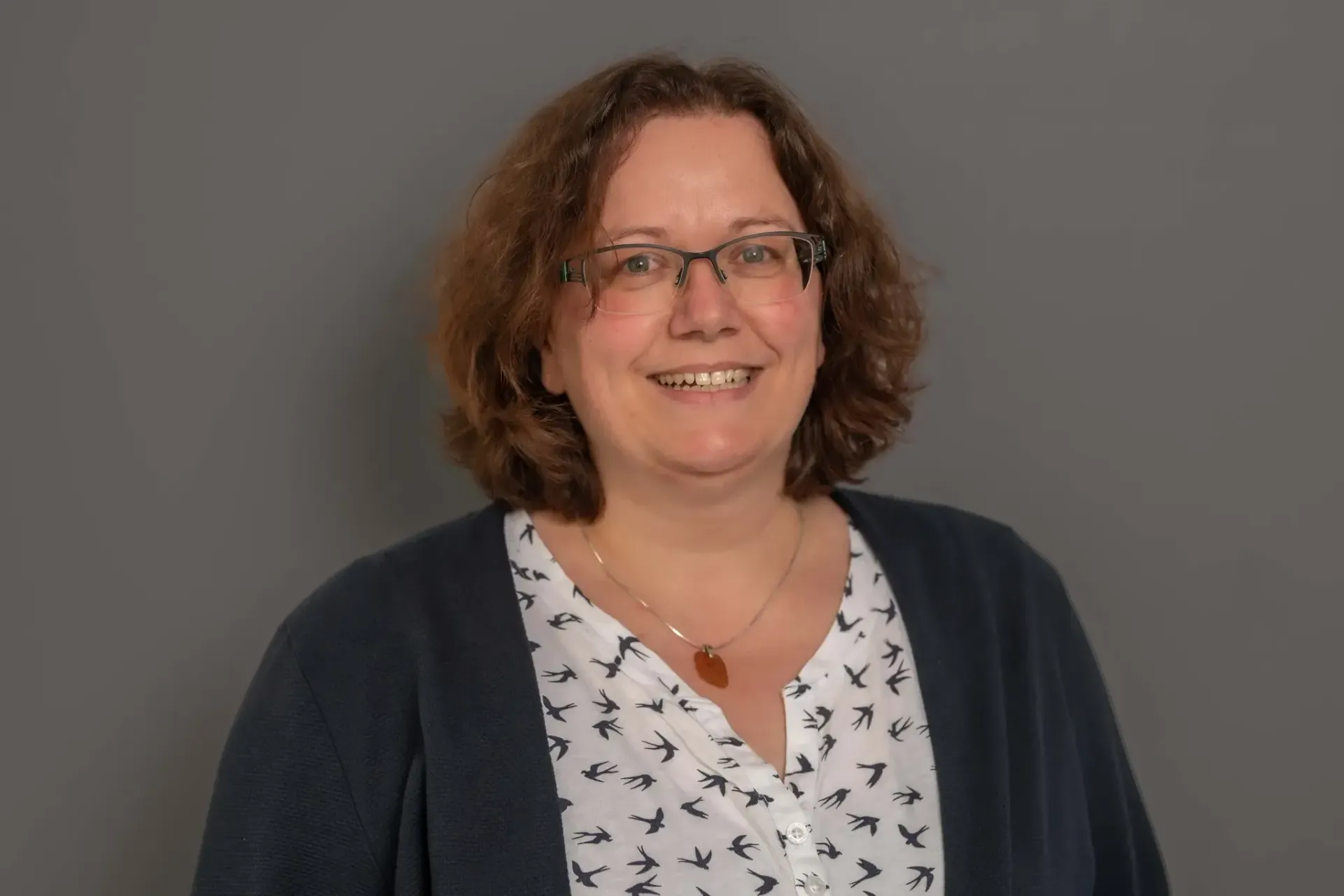 Eine Frau mit Brille und Pullover lächelt in die Kamera.