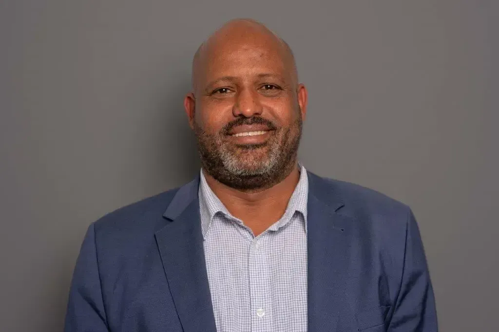 Ein kahlköpfiger Mann mit Bart trägt einen blauen Anzug und lächelt in die Kamera.