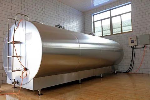 Un gran tanque de acero inoxidable está sentado en una habitación al lado de una ventana.