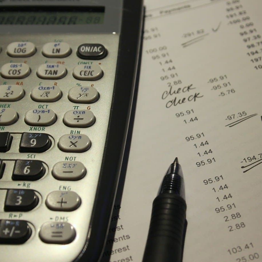 Calculadora, bolígrafo y documentos financieros con notas manuscritas sobre un escritorio.