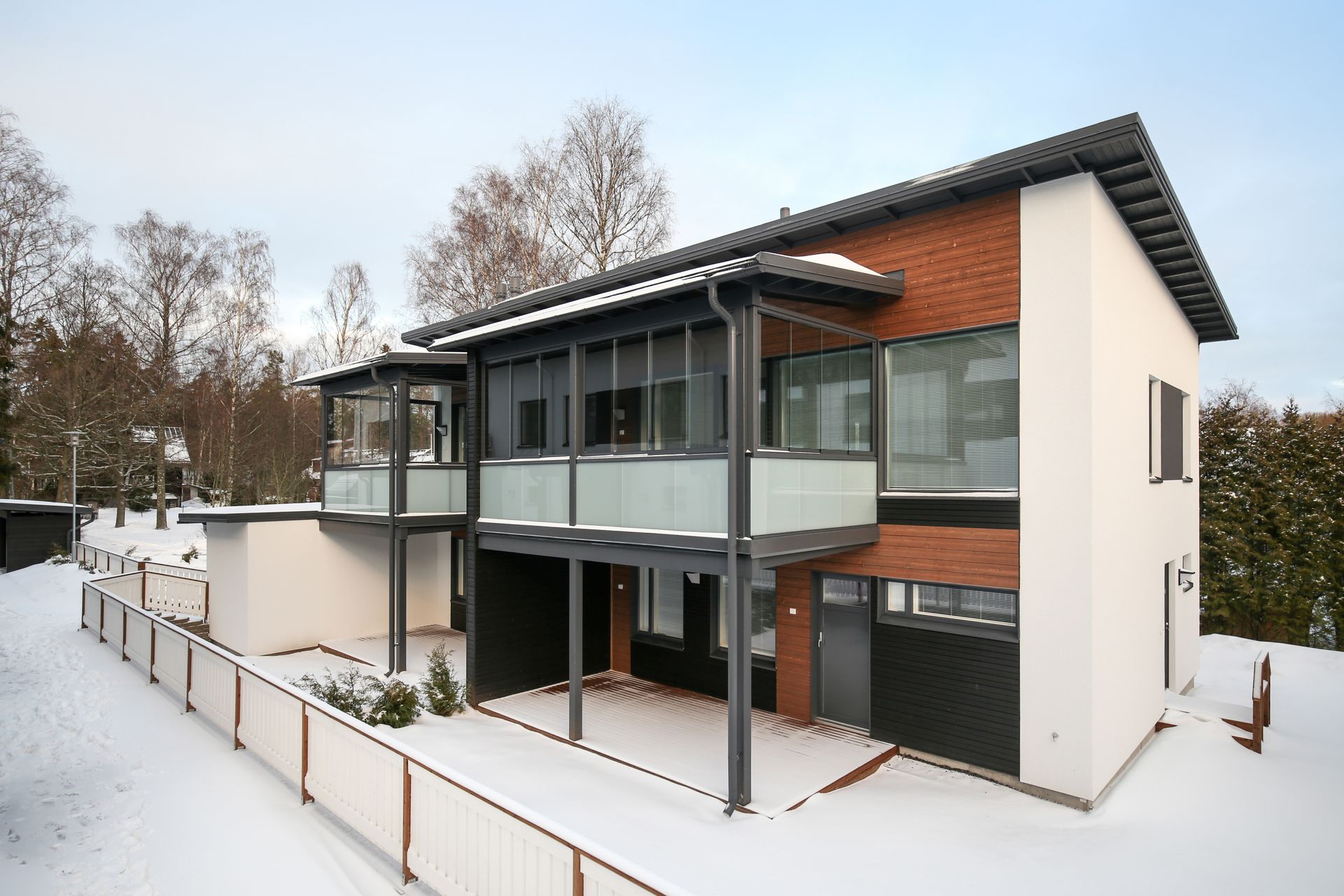 Lumipeitteinen moderni kaksikerroksinen talo, jossa on suuret ikkunat ja katettu terassi