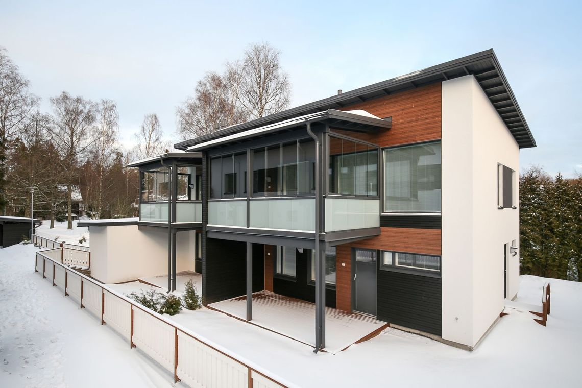Lumipeitteinen moderni kaksikerroksinen talo, jossa on suuret ikkunat ja katettu terassi