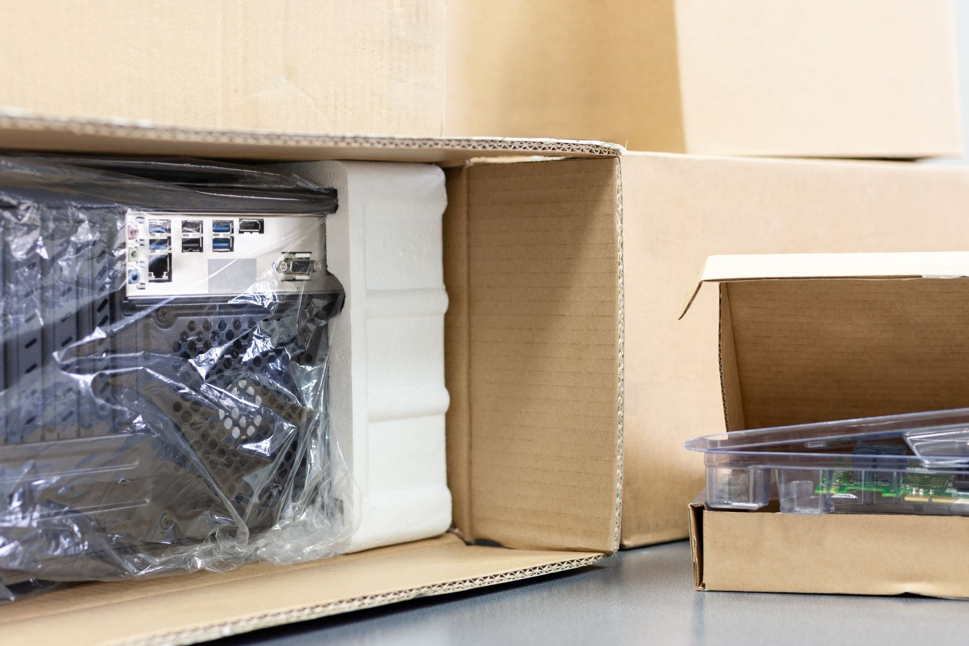 Une tour d'ordinateur emballée dans du carton et de la mousse, avec à côté une petite boîte ouverte contenant une carte de circuit imprimé.