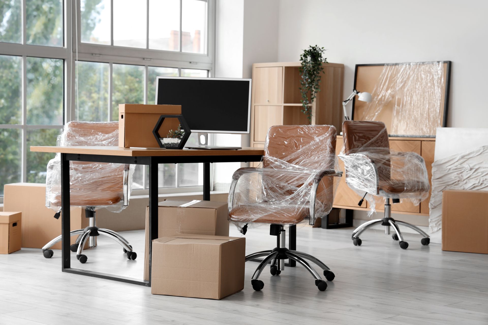 Un espace de travail de bureau en cours de déménagement, avec des chaises et des meubles emballés dans du plastique et des cartons posés au sol.
