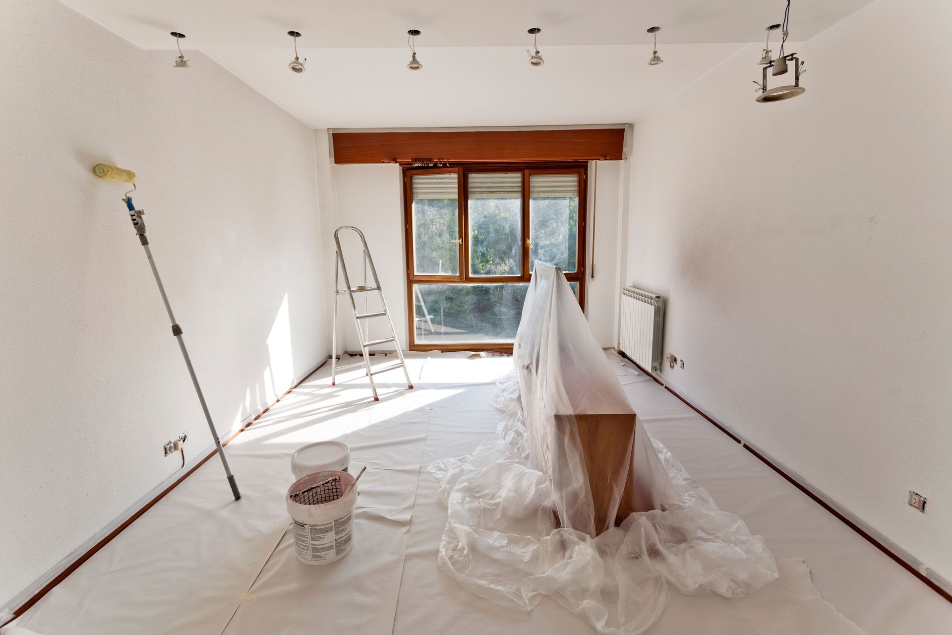 Pièce lumineuse et vide en cours de rénovation, avec bâches de protection, échelle et lumière naturelle.