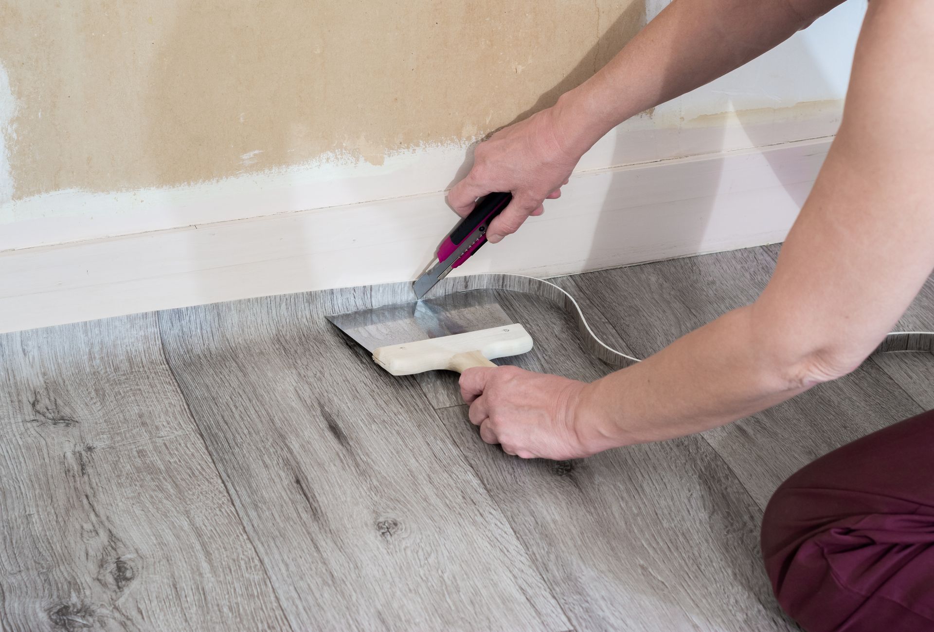 Une personne utilise un rouleau à peinture pour appliquer de la peinture blanche le long d'une plinthe sur un sol gris.