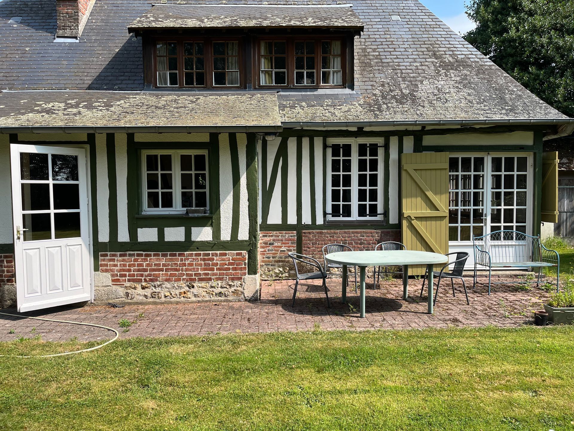 Extérieur de chalet rustique avec des boiseries blanches et vertes, un muret en briques, une table de patio et un premier plan gazonné.