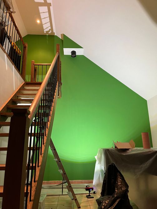 Escalier longeant un mur vert vif dans une pièce en rénovation, avec échelle et meubles recouverts.
