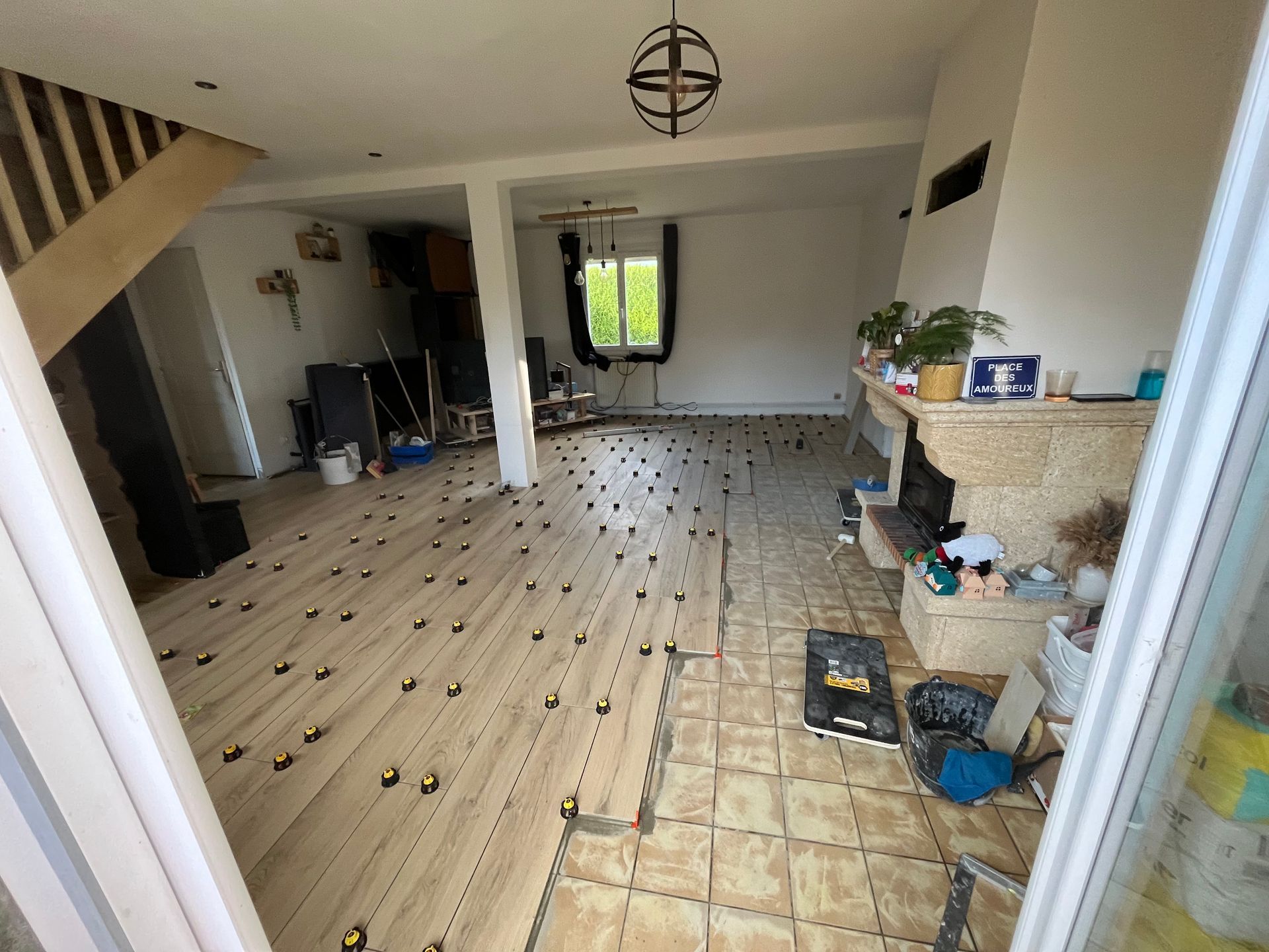 Salon vide en cours de rénovation, avec parquet clair, entrée carrelée et outils et matériaux éparpillés.