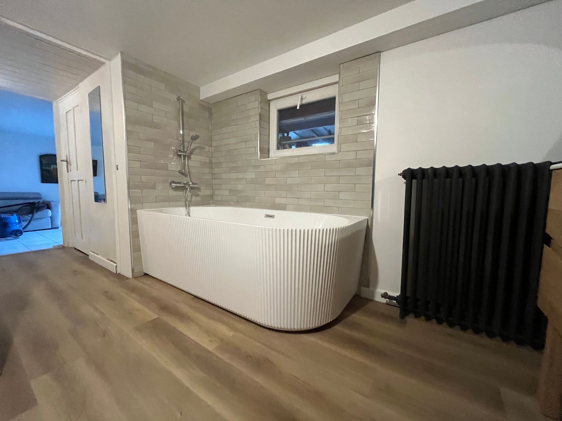Salle de bains moderne avec baignoire en îlot, mur carrelé, fenêtre et radiateur noir