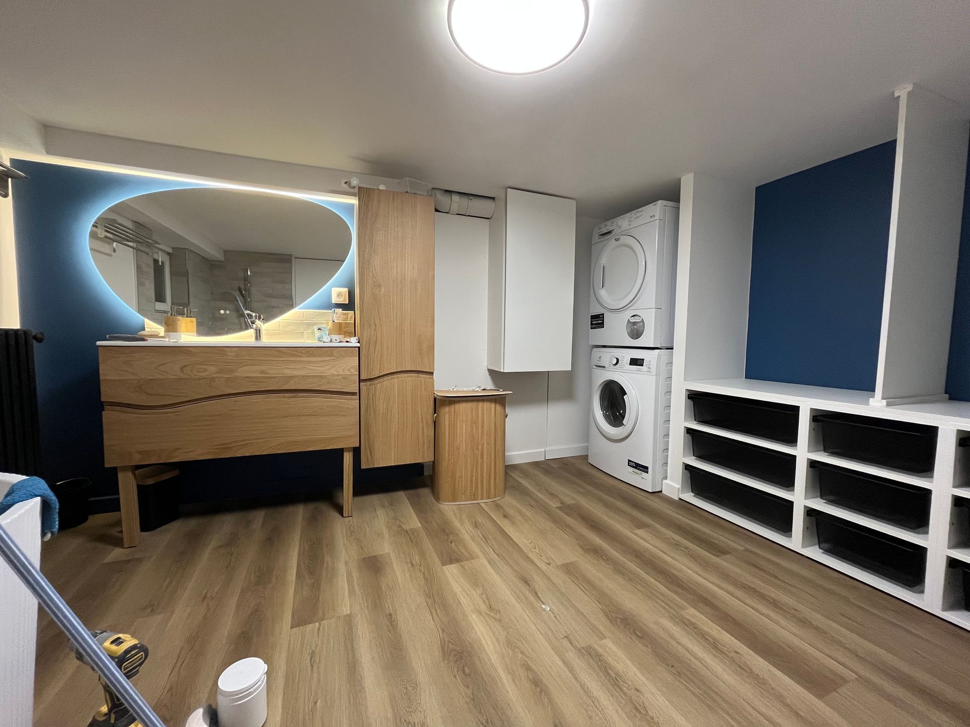 Chambre moderne avec coiffeuse en bois, murs bleus, étagères de rangement blanches et laveuse-sécheuse superposées