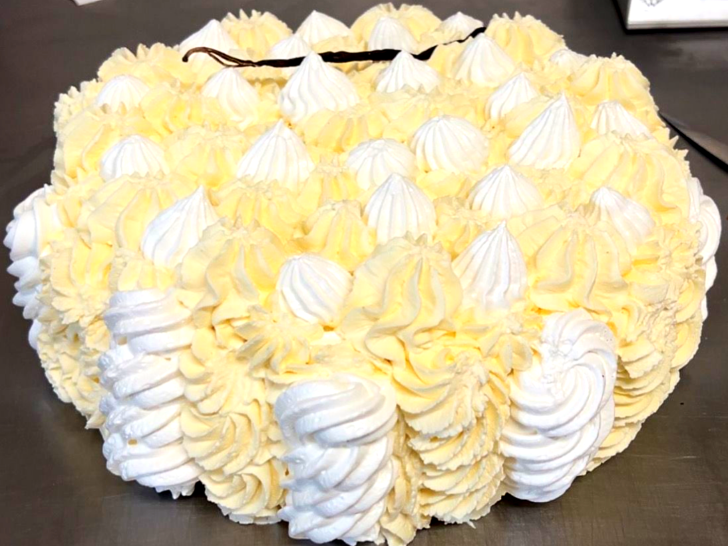 Gâteau glacé jaune et blanc avec des tourbillons, un glaçage en poche et une gousse de vanille.