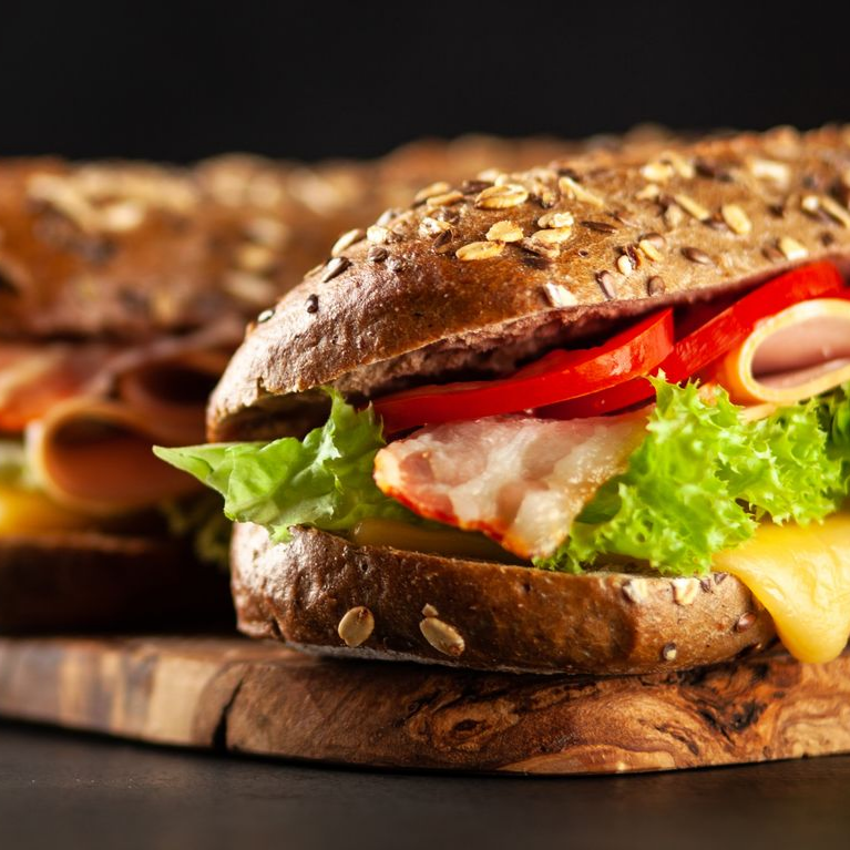 Sandwich sur une planche de bois avec bacon, tomate, laitue et fromage sur un pain aux graines.