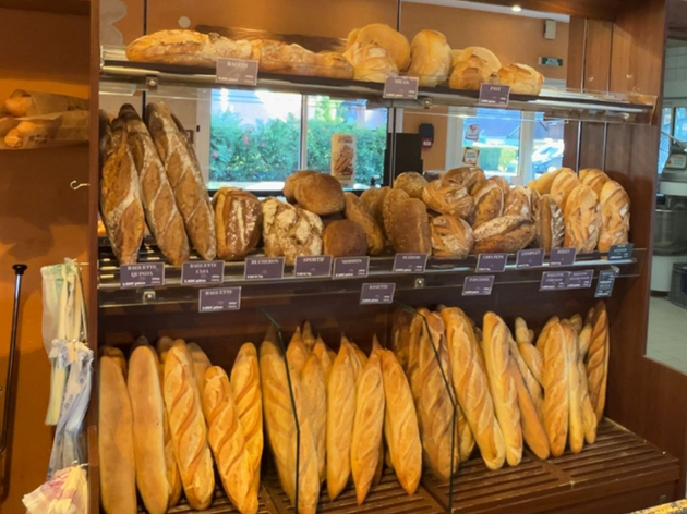 Présentoir de boulangerie de divers pains, baguettes et petits pains sur des étagères en bois.