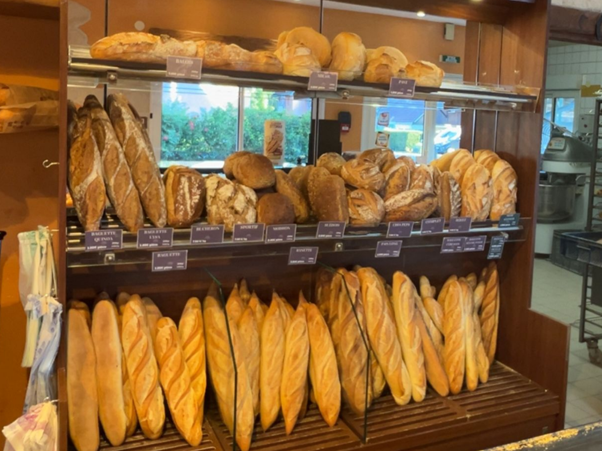 Présentoir à pain dans une boulangerie avec différents pains et baguettes sur des étagères en bois.