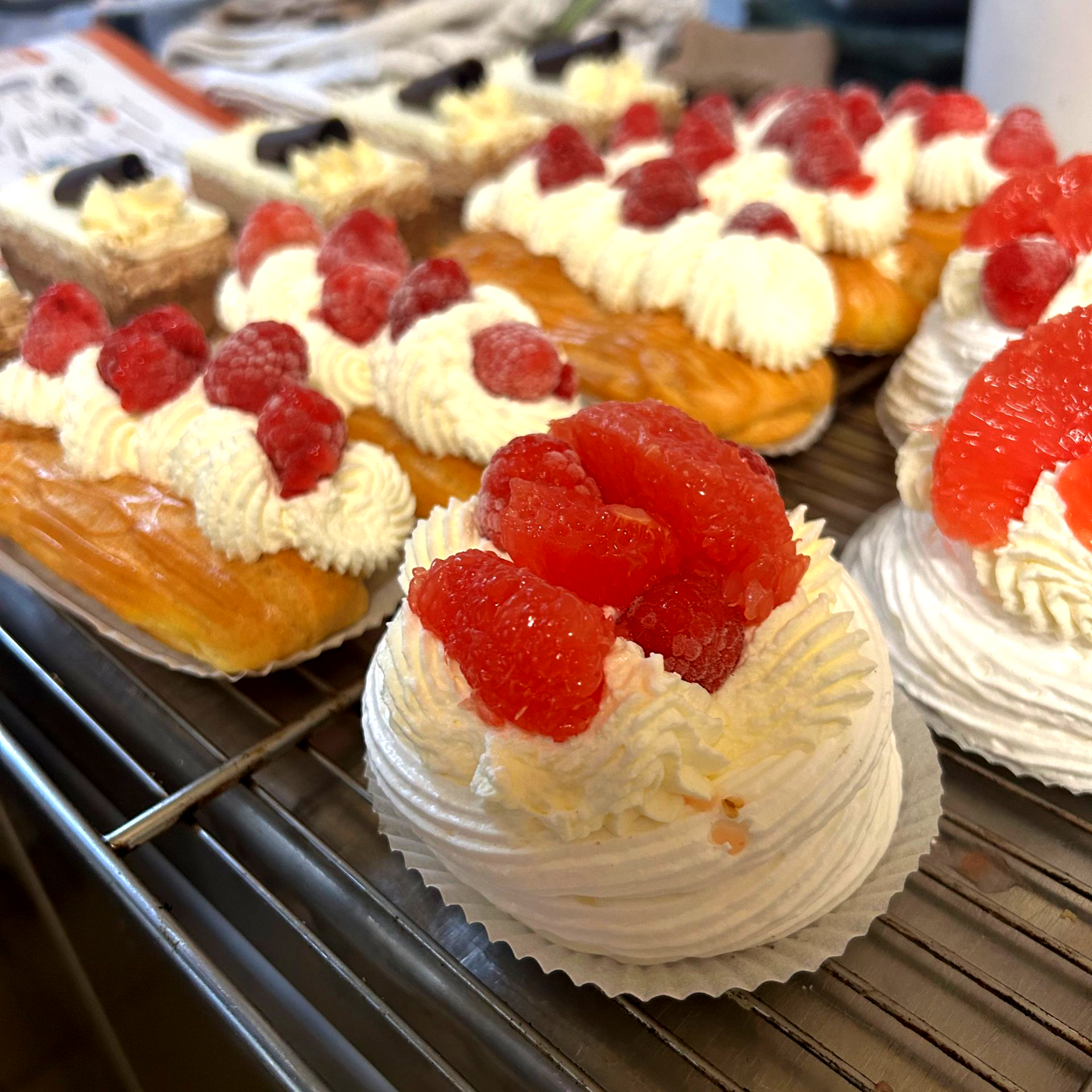 Pâtisseries garnies de crème fouettée et de fruits rouges sur une grille.