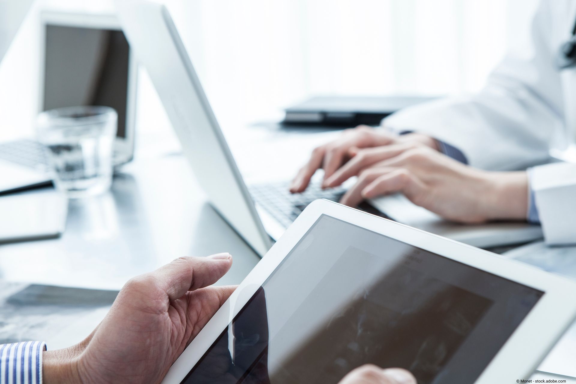 Ein Kunde schaut etwas auf einem Tablet nach, ein Steuerberater tippt währenddessen etwas auf dem Tablet ein