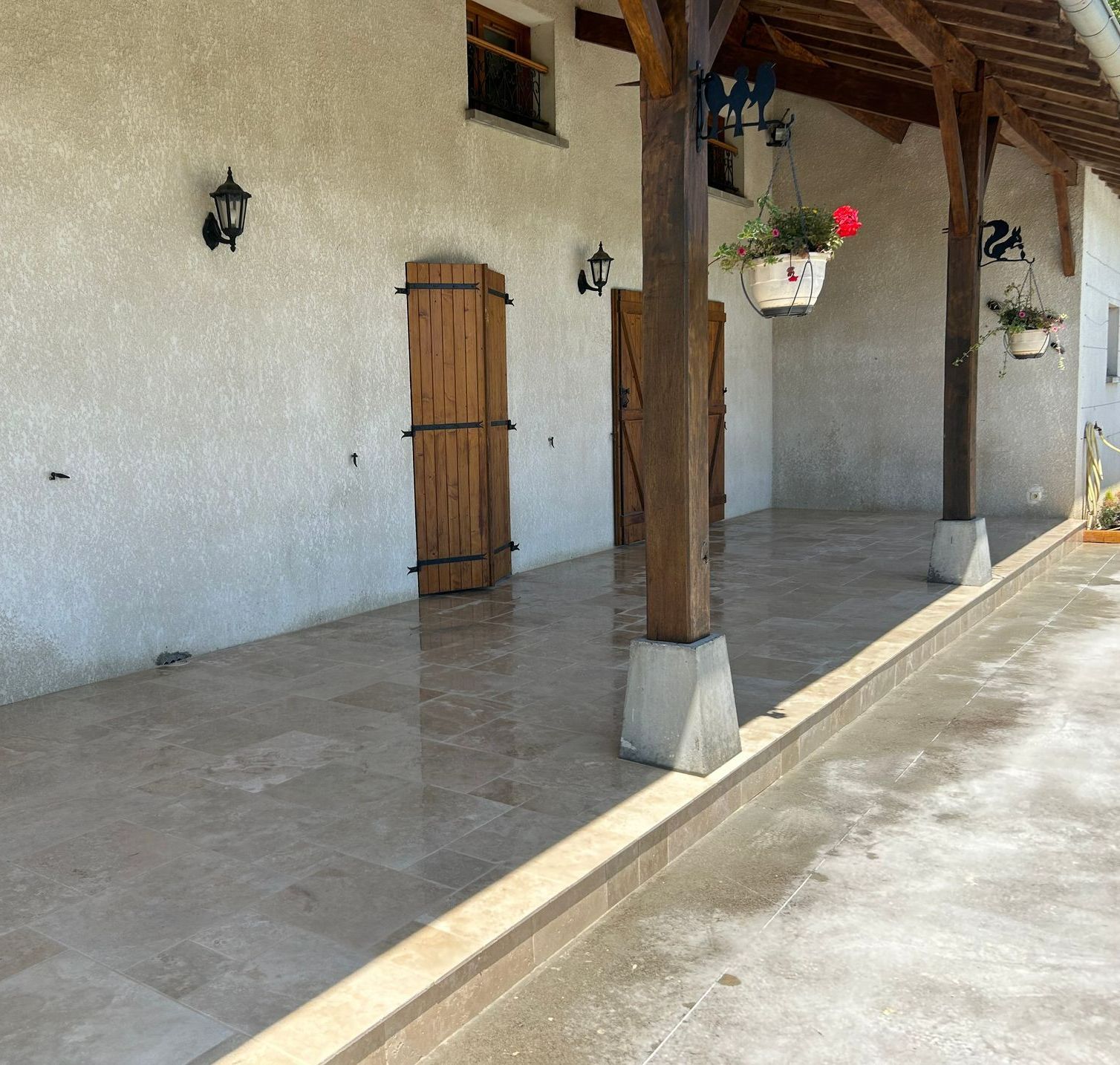 Une terrasse en carrelage grès cérame devant une maison avec des volets en bois.