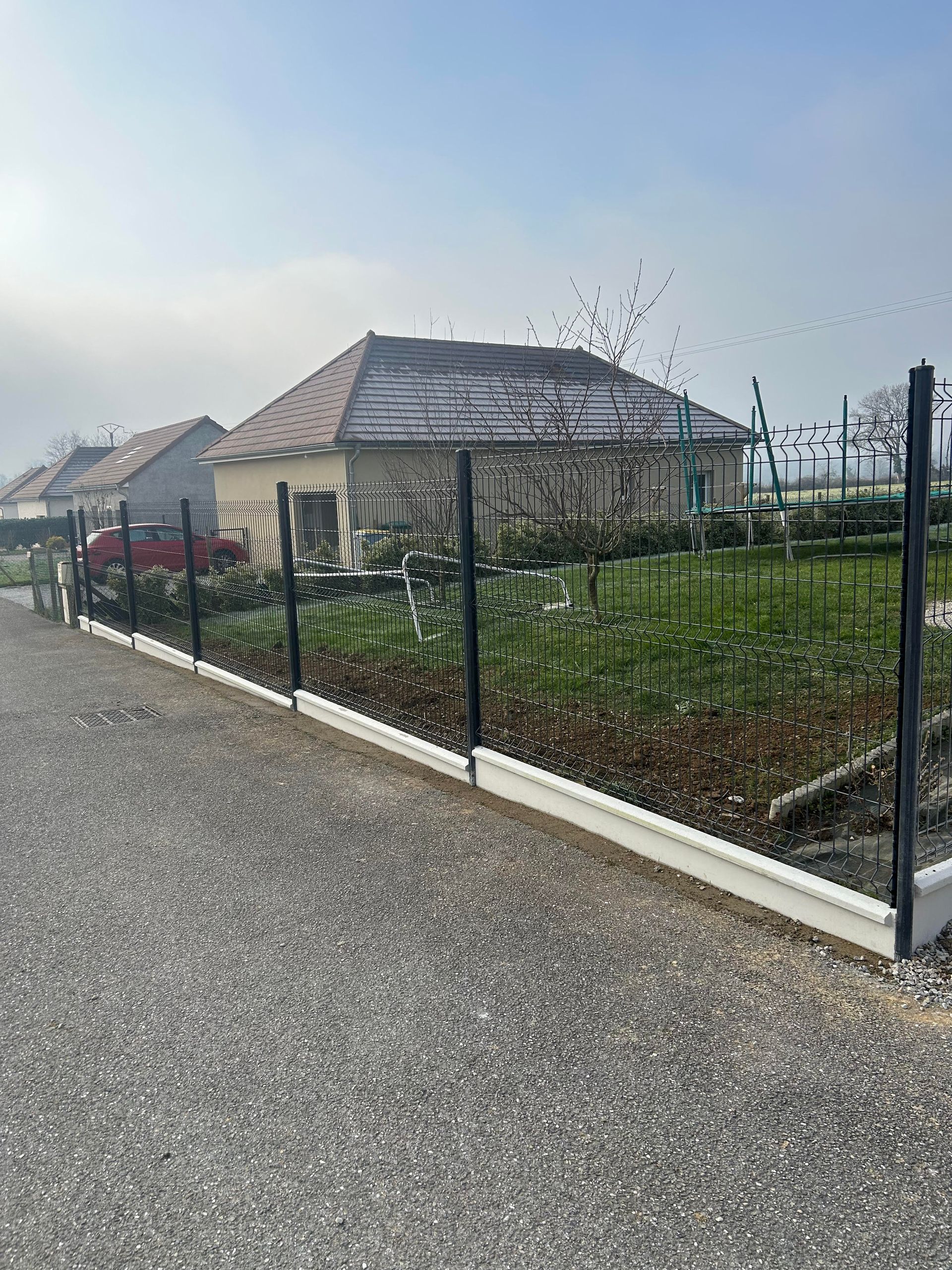 Un grillage devant une maison avec un jardin.