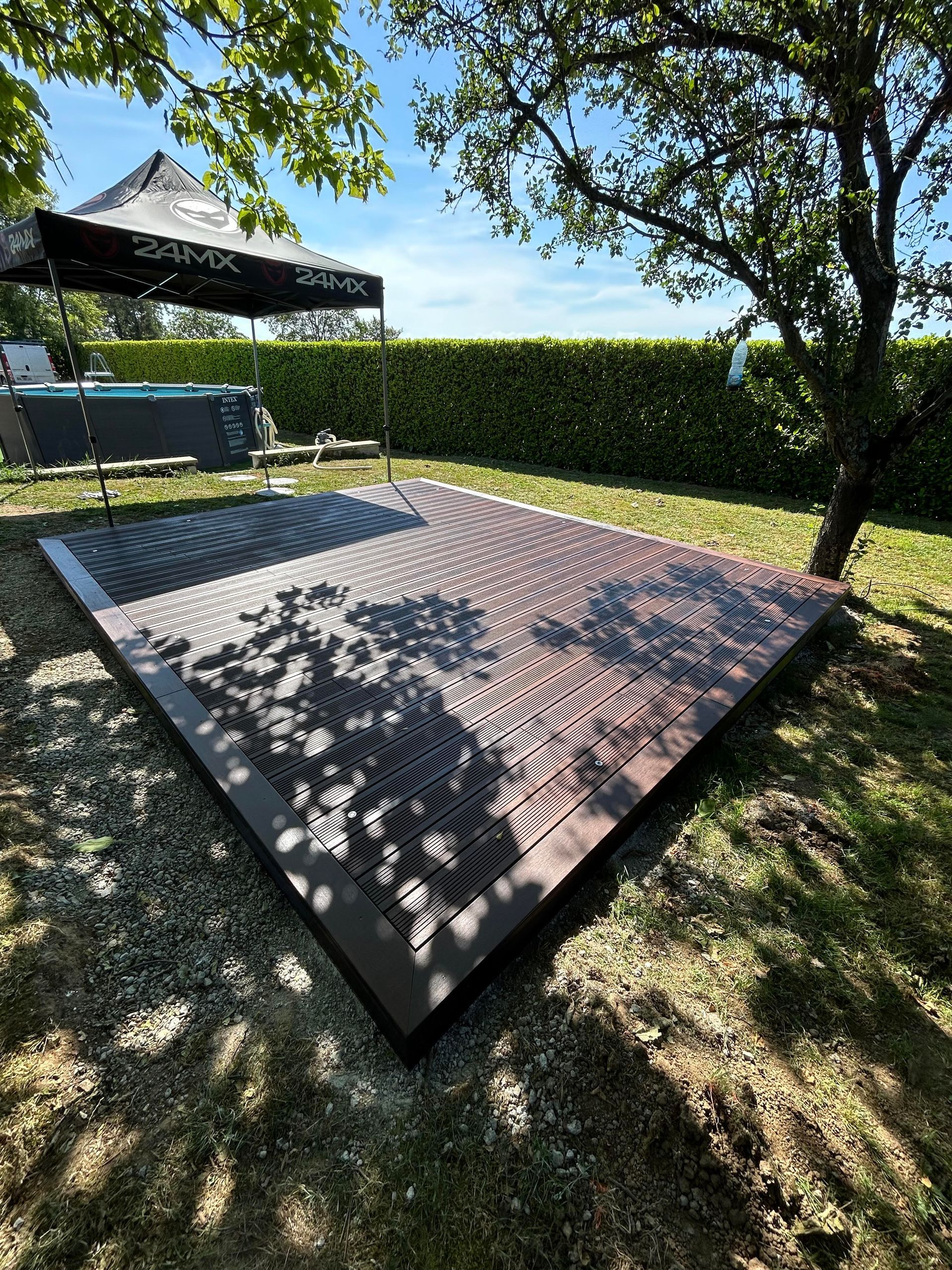 Une terrasse en bois dans un jardin, installée sous un arbre.