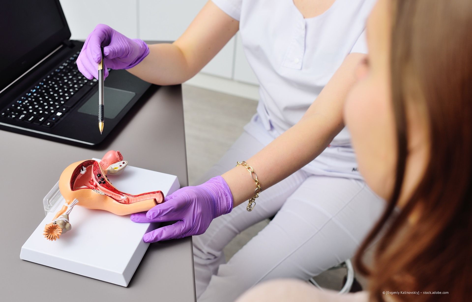 Medizinische Fachkraft mit violetten Handschuhen demonstriert die Anatomie anhand eines Beckenskelettmodells an einem Schreibtisch