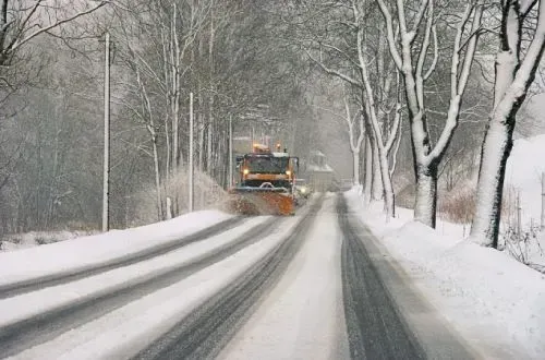 Ein Schneepflug fährt eine schneebedeckte Straße entlang.