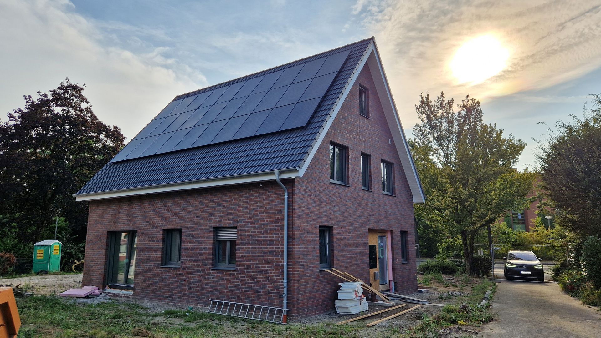 Rotes Backsteinhaus mit Solarzellen auf dem Dach. Auf der Einfahrt parkt ein Auto.