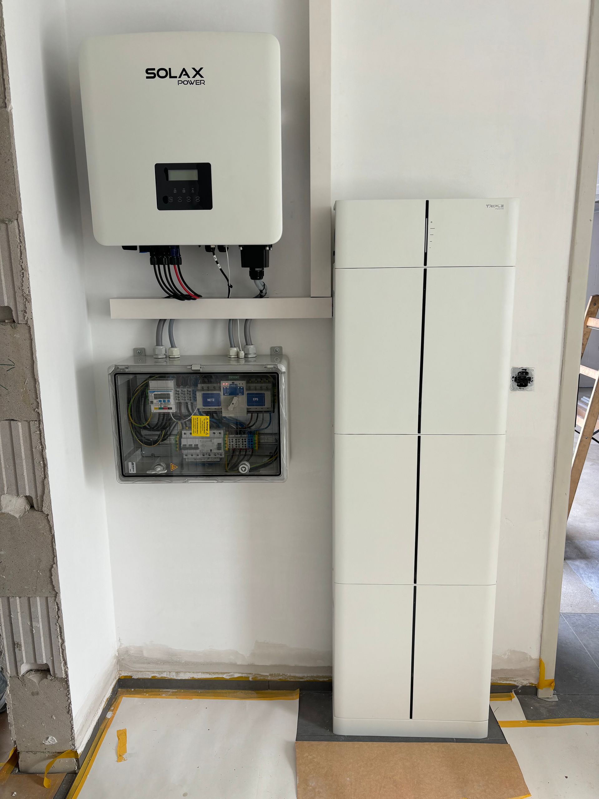 Weißer Solarwechselrichter und Batteriesystem an einer Wand installiert, darunter ein Schaltschrank.