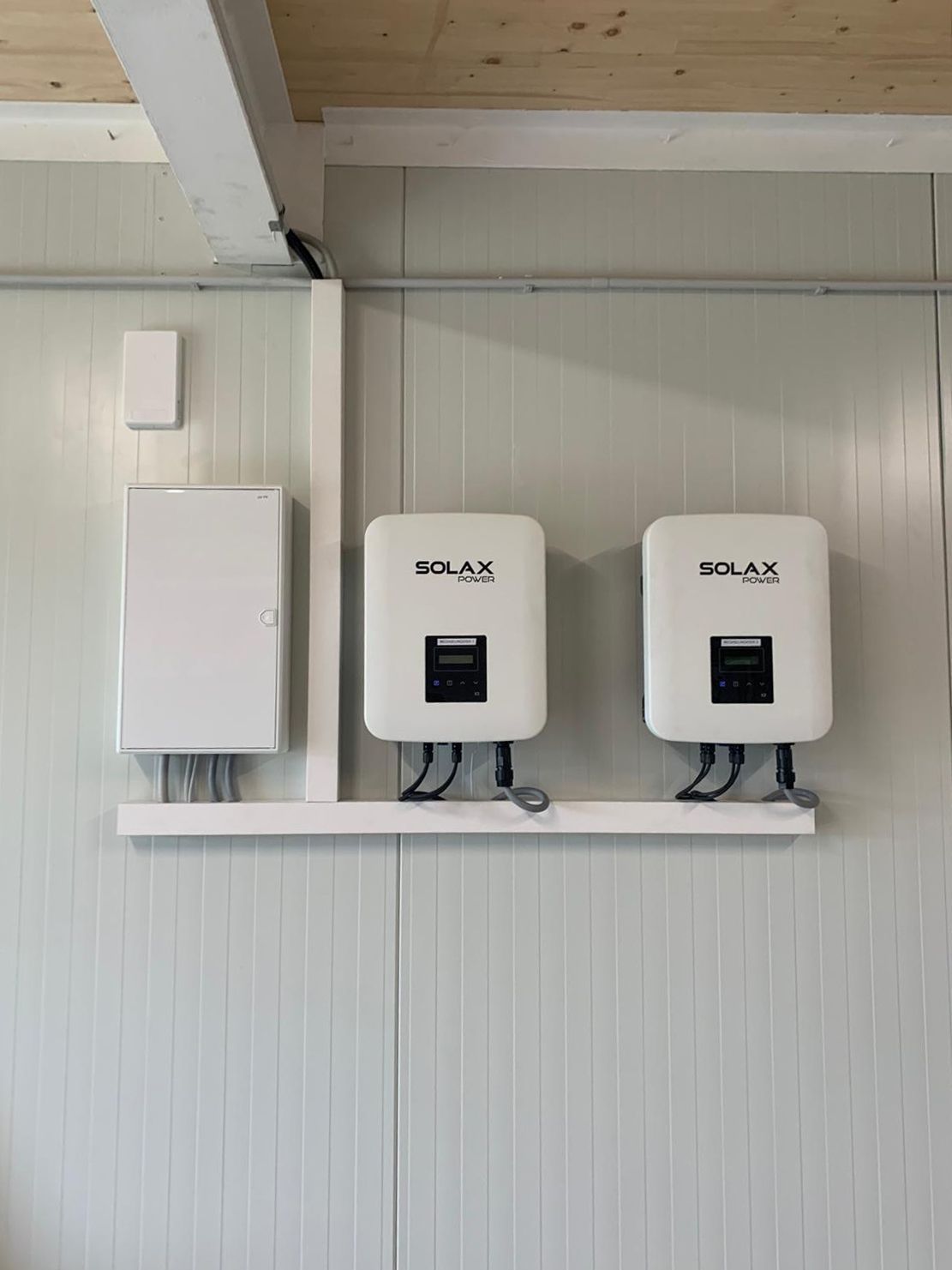Zwei weiße Solarwechselrichter, an einer Wand neben einem weißen Schaltkasten montiert.