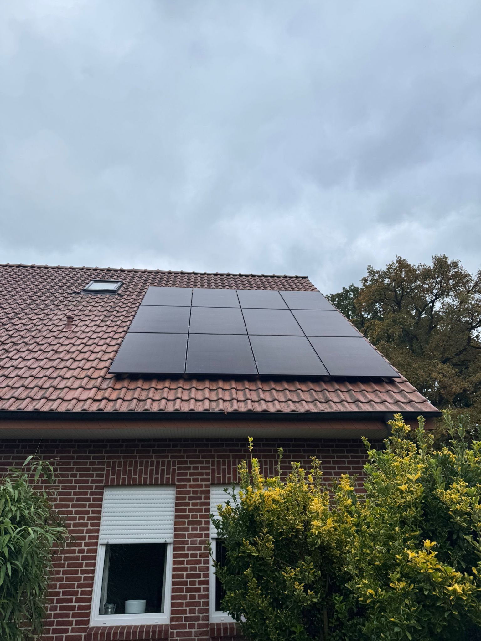 Sonnenkollektoren auf dem roten Ziegeldach eines Backsteinhauses an einem bewölkten Tag.