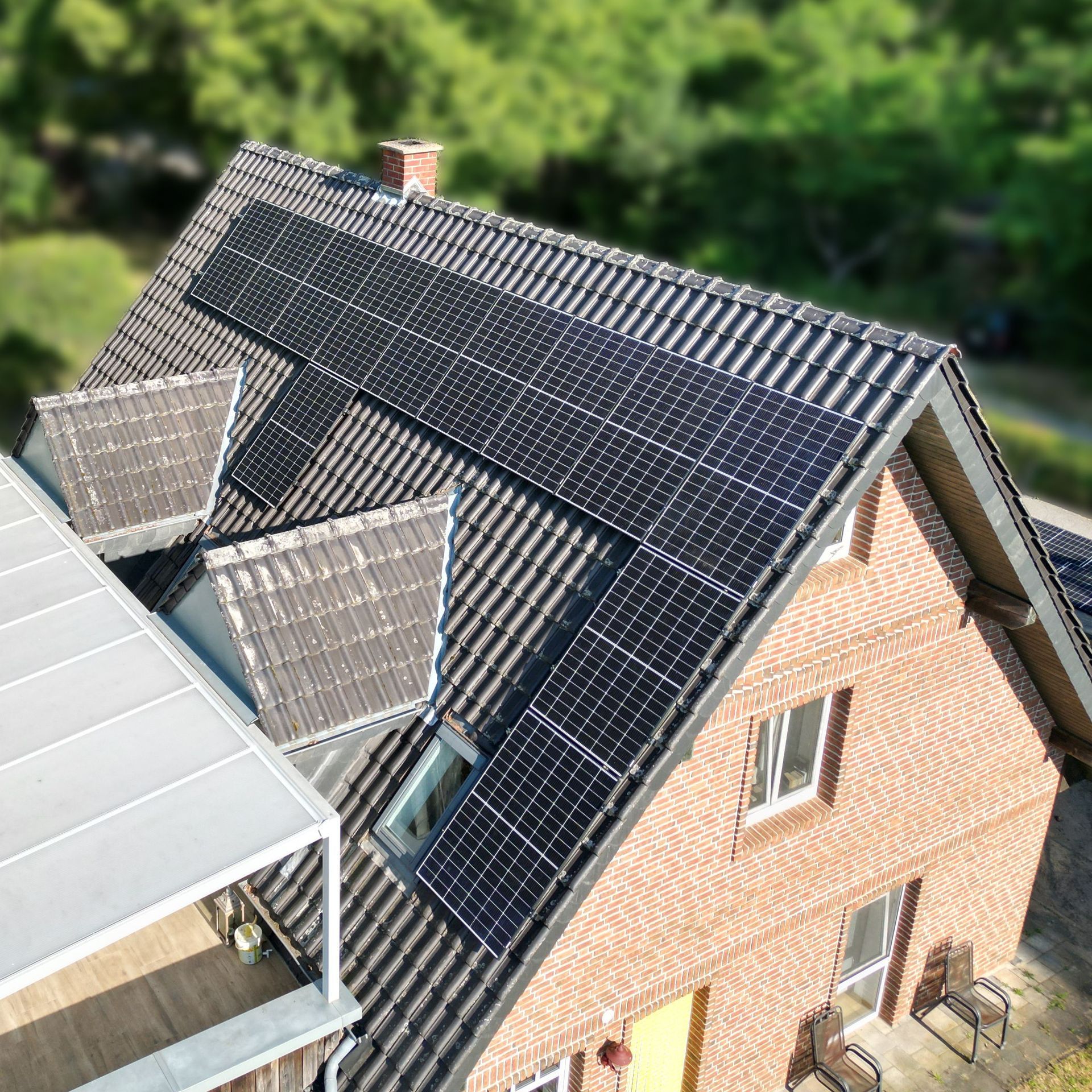 Rotes Backsteinhaus mit Solarmodulen auf dem Dach. Zwei Oberlichter und eine weiße Markise.