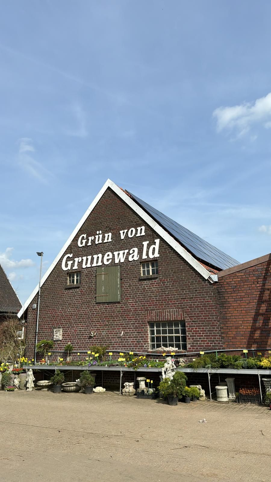 Backsteingebäude mit „Grün von Grunewald“-Schriftzug, Solaranlage auf dem Dach, Schaufenster davor.