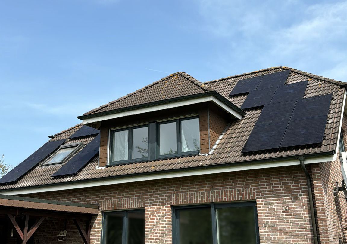 Auf dem Ziegeldach eines Backsteinhauses vor blauem Himmel installierte Solarmodule.